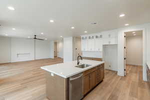 Kitchen featuring stainless steel dishwasher, ceiling fan, sink, white cabinets, and an island with sink