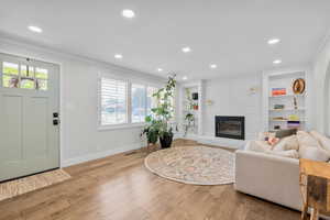 Living room featuring built in shelves, light wood-type flooring, a brick fireplace, and ornamental molding