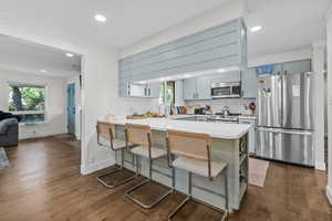 Kitchen with dark hardwood / wood-style flooring, backsplash, kitchen peninsula, a breakfast bar, and appliances with stainless steel finishes