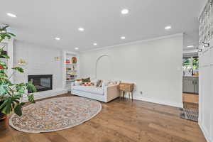 Living room featuring a brick fireplace, ornamental molding, sink, built in features, and hardwood / wood-style floors