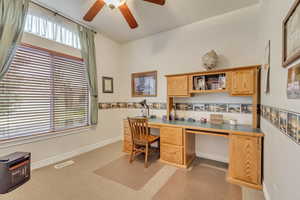 Home office, ceiling fan, light colored carpet, and desk