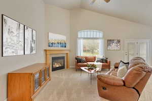 Living room with ceiling fan, light carpet, high vaulted ceiling, and a tiled fireplace
