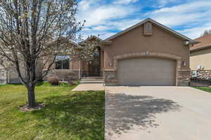 View of front facade with stucco siding, stone siding, a front lawn, an attached garage, and driveway