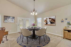 Dining area with a notable chandelier, lofted ceiling, and light carpet