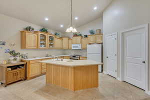 Kitchen featuring light brown cabinetry, white appliances, sink, a center island with sink, and a chandelier