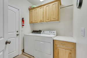 Laundry room with washing machine and dryer, light tile patterned flooring, and cabinets
