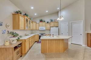 Kitchen featuring light brown cabinets, white appliances, a center island with sink, and an inviting chandelier