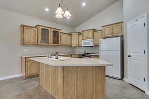 Kitchen with glass insert cabinets, light countertops, white appliances, a center island with sink, and light tile patterned flooring