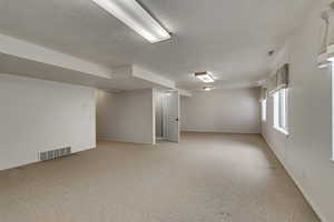 Below grade area with light carpet, baseboards, visible vents, and a textured ceiling
