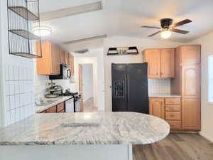 Kitchen with decorative backsplash, light wood-type flooring, vaulted ceiling, and black appliances