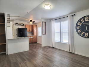 Kitchen with black fridge, dark hardwood / wood-style flooring, light stone counters, vaulted ceiling, and decorative backsplash