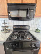 Room details featuring light stone countertops, decorative backsplash, and black appliances