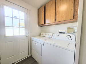 Clothes washing area featuring washer and dryer, dark wood-type flooring, and cabinets