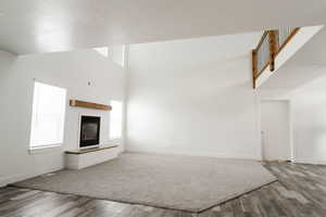 Unfurnished living room featuring hardwood / wood-style floors, a towering ceiling, and a textured ceiling