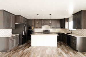 Kitchen with dark hardwood / wood-style flooring, black appliances, sink, decorative light fixtures, and a kitchen island