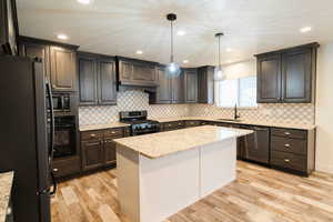 Kitchen with light stone countertops, sink, a center island, hanging light fixtures, and appliances with stainless steel finishes