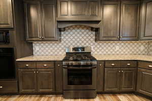 Kitchen featuring black appliances, ventilation hood, decorative backsplash, light wood-type flooring, and dark brown cabinets