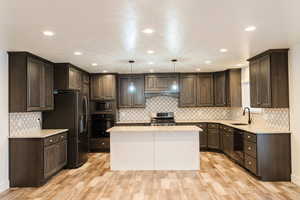 Kitchen featuring black appliances, sink, light wood-type flooring, decorative light fixtures, and a kitchen island