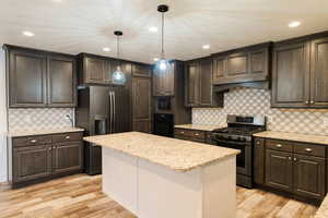 Kitchen with appliances with stainless steel finishes, light wood-type flooring, dark brown cabinets, pendant lighting, and a kitchen island