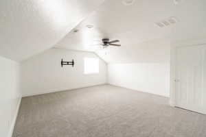 Additional living space with vaulted ceiling, ceiling fan, carpet flooring, and a textured ceiling