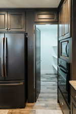 Kitchen with light stone countertops, built in microwave, light hardwood / wood-style flooring, stainless steel fridge, and black oven