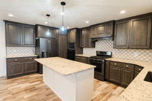 Kitchen featuring decorative light fixtures, stainless steel appliances, light stone counters, and light hardwood / wood-style flooring