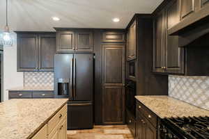 Kitchen with hanging light fixtures, stainless steel fridge, light stone countertops, light wood-type flooring, and tasteful backsplash