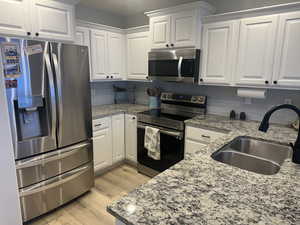 Kitchen with decorative backsplash, white cabinetry, sink, and stainless steel appliances