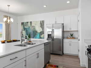 Kitchen featuring light wood-type flooring, stainless steel appliances, sink, white cabinets, and a chandelier