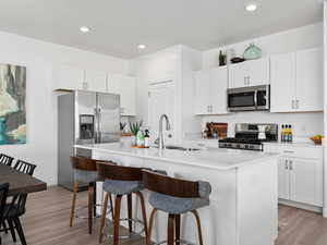 Kitchen featuring stainless steel appliances, sink, a center island with sink, light hardwood / wood-style flooring, and white cabinetry