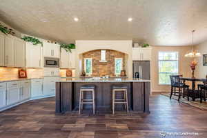 Kitchen featuring light stone countertops, backsplash, a center island with sink, white cabinets, and appliances with stainless steel finishes