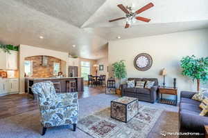 Carpeted living room featuring ceiling fan, lofted ceiling, and a textured ceiling