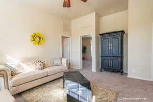 Living room with ceiling fan, light colored carpet, a textured ceiling, and a high ceiling