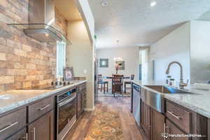 Kitchen with sink, wall chimney exhaust hood, light stone countertops, a textured ceiling, and stainless steel appliances