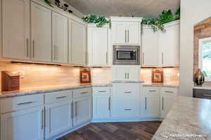 Kitchen with tasteful backsplash, light stone counters, stainless steel microwave, and white cabinets