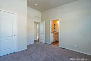 Unfurnished bedroom with ensuite bathroom, a towering ceiling, and light colored carpet