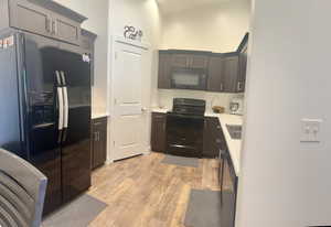 Kitchen with light wood finished floors, black appliances, light countertops, and a sink