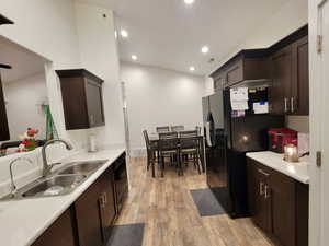 Kitchen featuring dark brown cabinetry, sink, black appliances, and light wood-type flooring