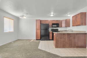 Kitchen featuring black appliances, light colored carpet, and a chandelier