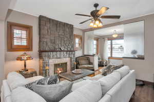 Living room with ceiling fan, a stone fireplace, ornamental molding, and wood-type flooring