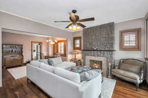 Living room with ceiling fan with notable chandelier, a fireplace, plenty of natural light, and dark wood-type flooring