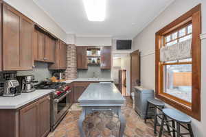 Kitchen featuring premium stove, backsplash, a center island, sink, and light tile patterned flooring