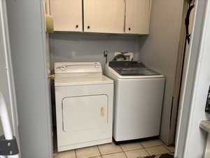 Washroom with cabinets, washing machine and dryer, and light tile patterned floors