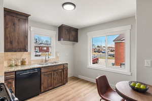 Kitchen with dark brown cabinetry, light stone countertops, dishwasher, sink, and light hardwood / wood-style floors