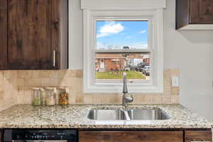 Kitchen with light stone countertops, tasteful backsplash, dark brown cabinetry, sink, and dishwasher