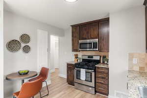 Kitchen with dark brown cabinets, light stone counters, stainless steel appliances, and tasteful backsplash