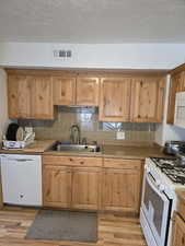 Kitchen with light hardwood / wood-style floors, white appliances, sink, and tasteful backsplash