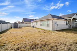 Rear view of property with central AC unit, a storage shed, and a lawn