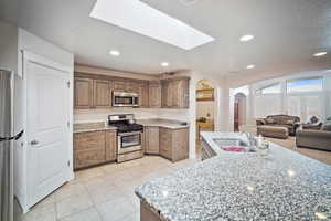 Kitchen with light stone countertops, sink, appliances with stainless steel finishes, and a skylight