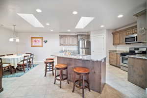 Kitchen featuring a skylight, light stone counters, stainless steel appliances, a kitchen island with sink, and sink